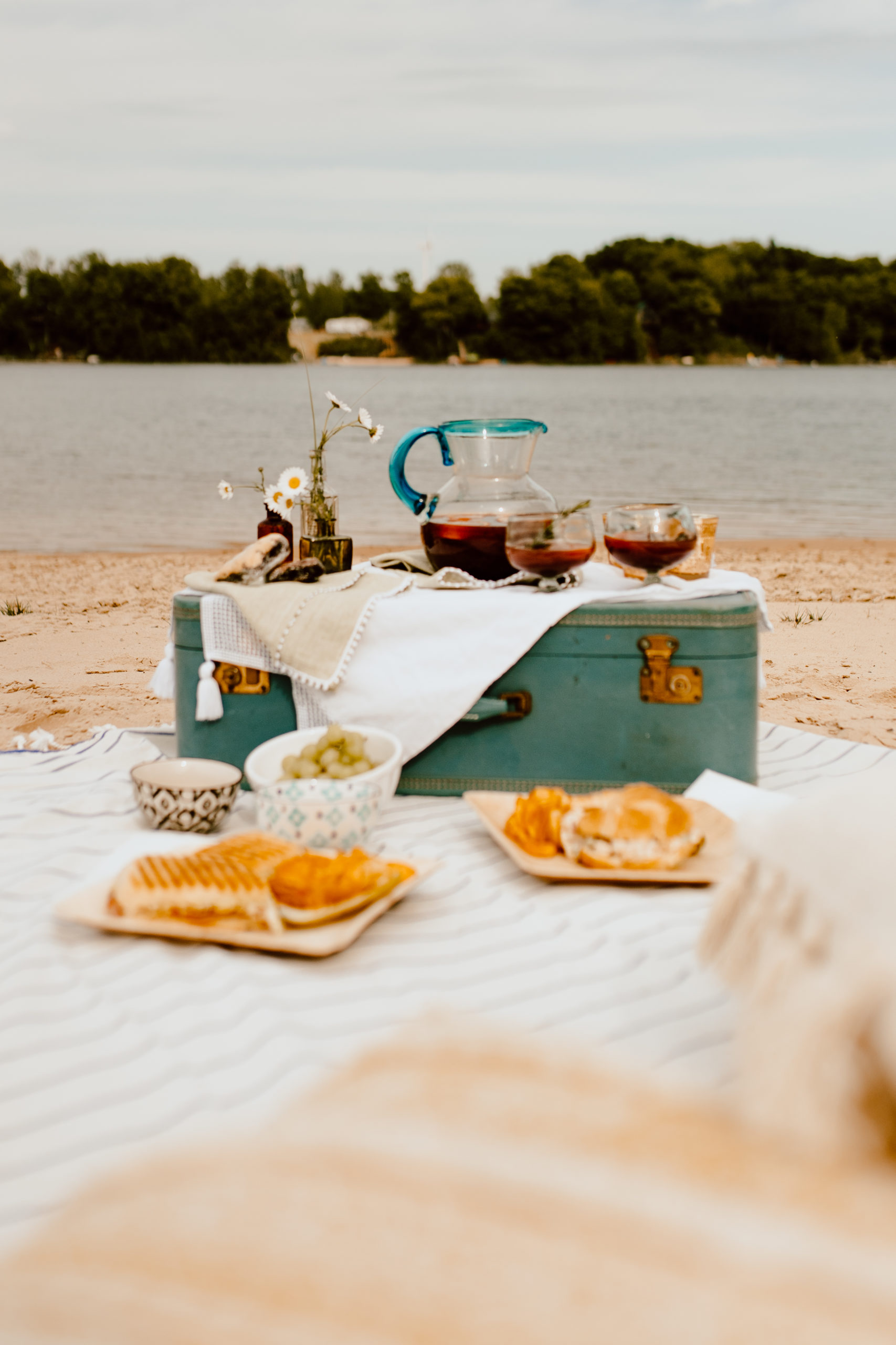 Beach picnic with vintage suitcase as a table. Sangria and sandwiches for food and comfy cushions for relaxing