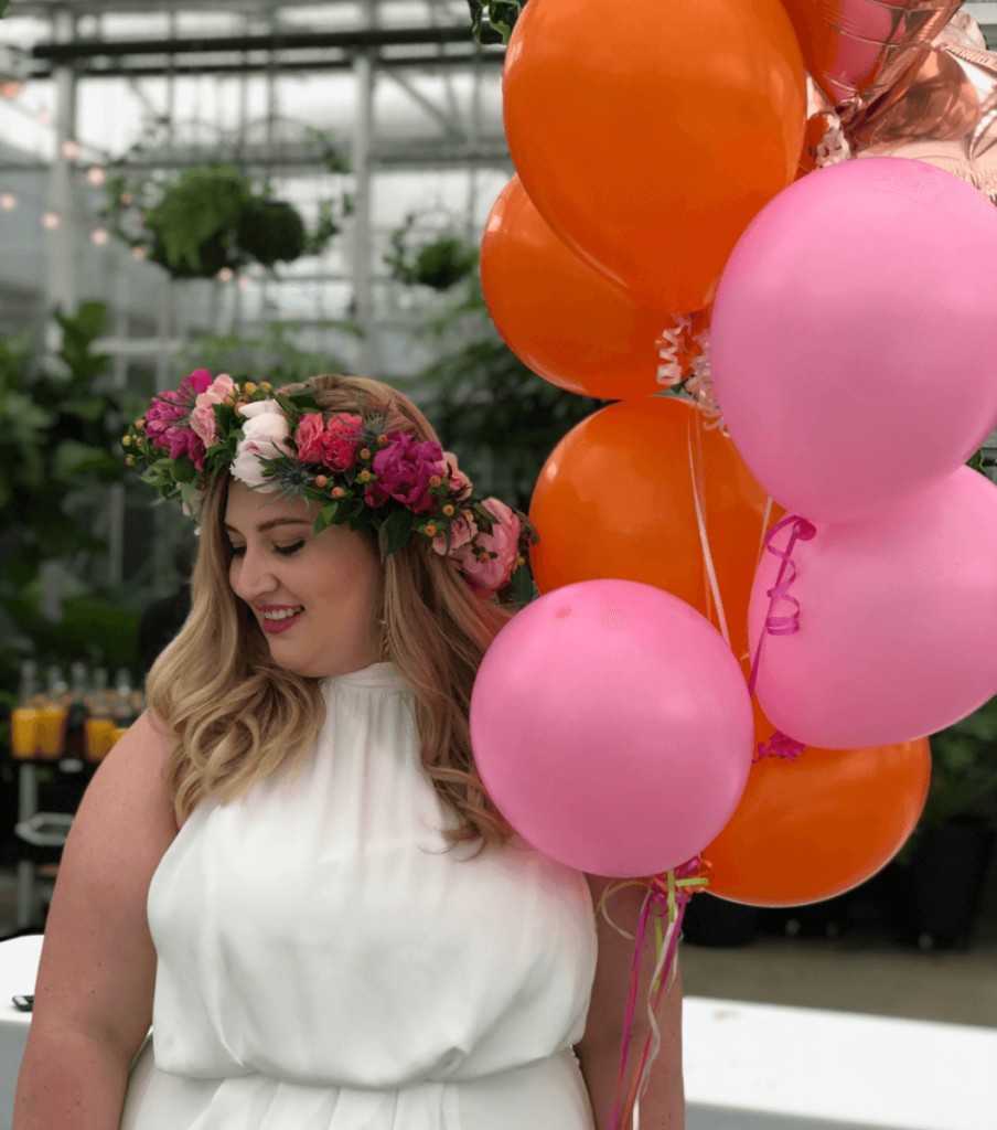 Bride to be wearing a floral crown holding brightly colored balloons in a greenhouse