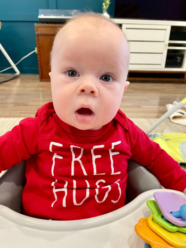 Red headed baby in a Free Hugs onesie.