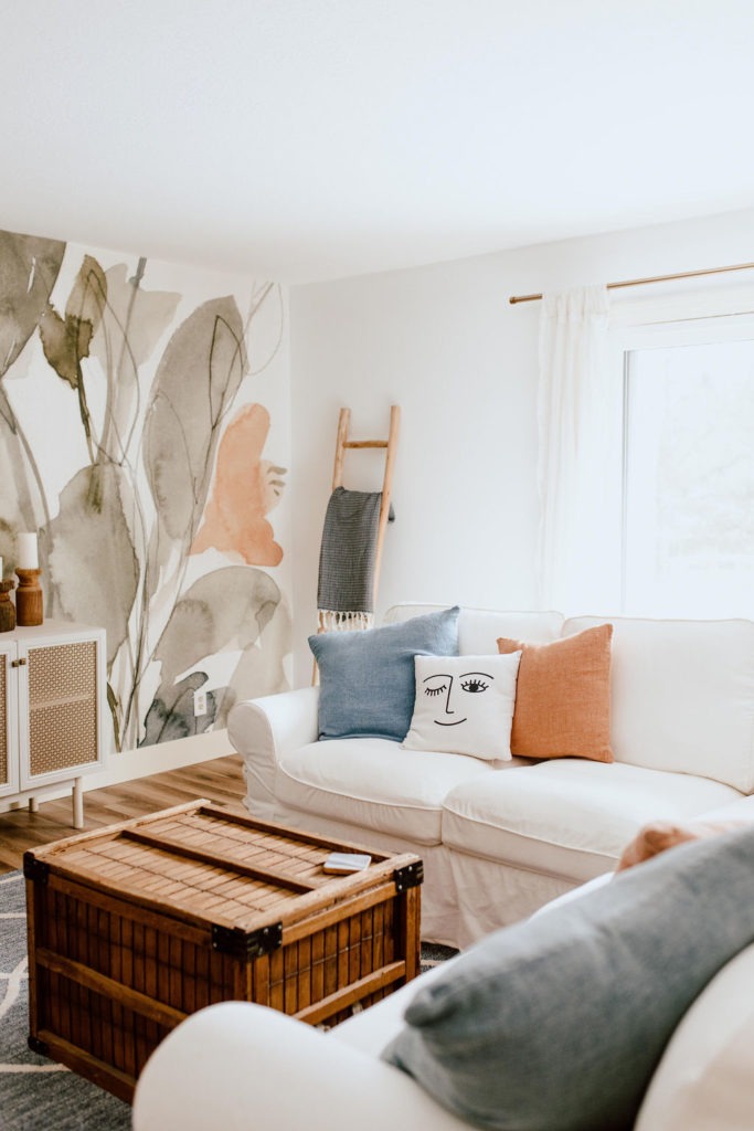 Living room featuring a large print mural, white sofa, blanket ladder and pillows.