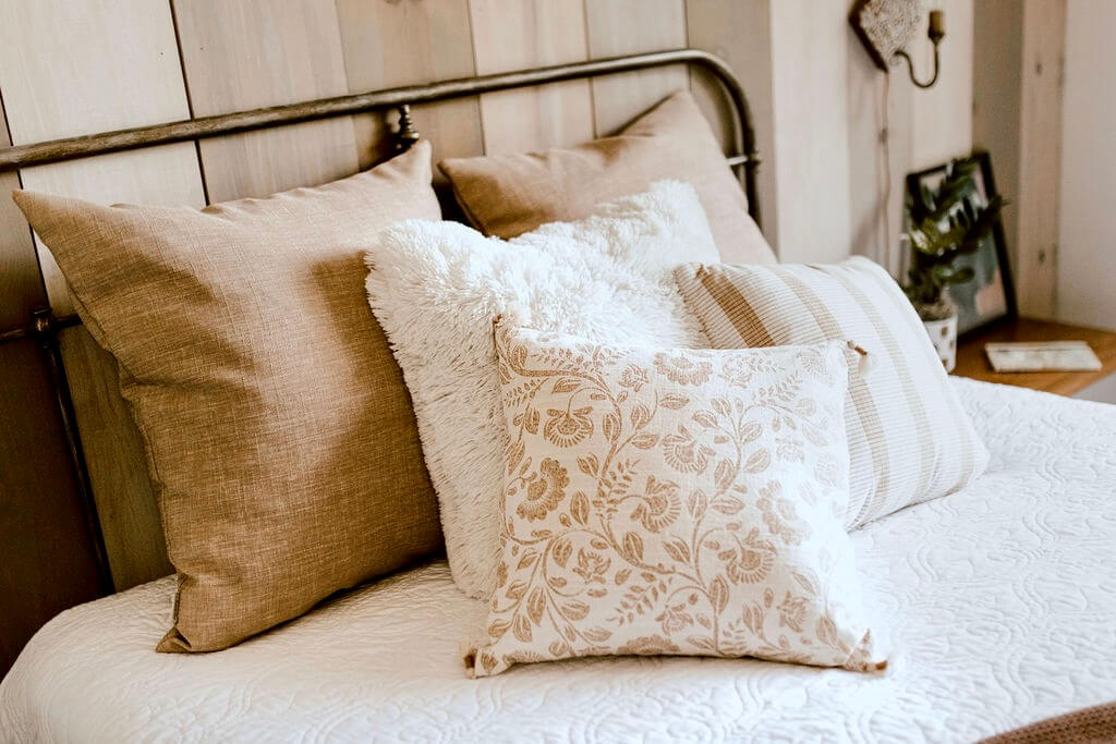 Assorted neutral, textured pillows on bed with white bedding.