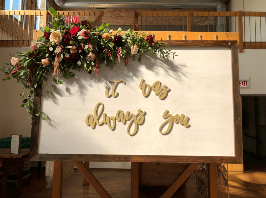 Wedding sign with large floral arch and the words "It was always you"