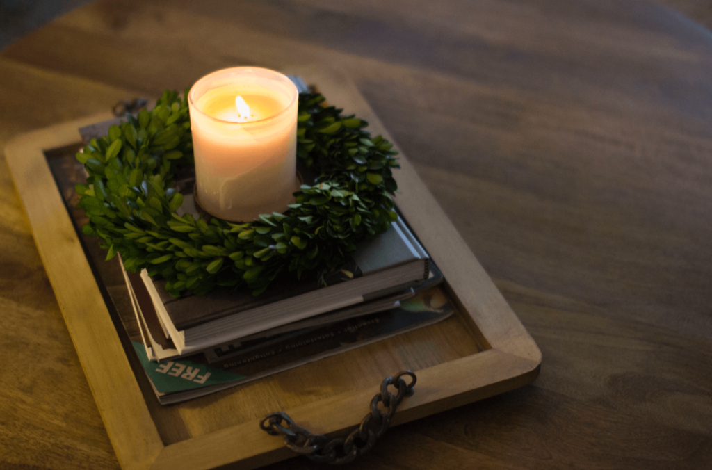 Simple wooden tray with a lit candle and small boxwood wreath.
