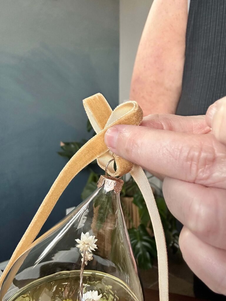 Tying a gold velvet ribbon on a Christmas ornament.