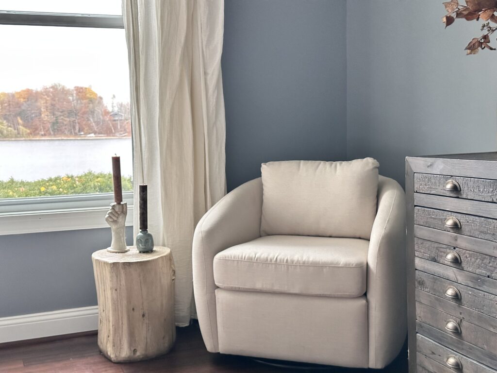 Cozy white chair in corner of bedroom with blue/grey walls.