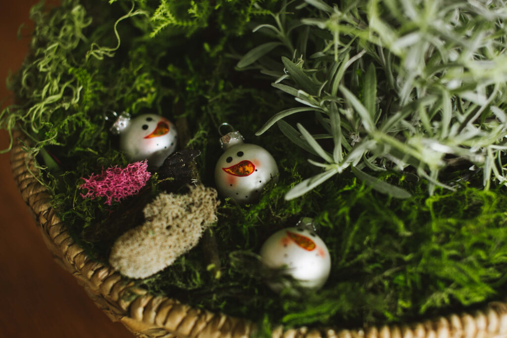 Bowl of moss with holiday ornaments.