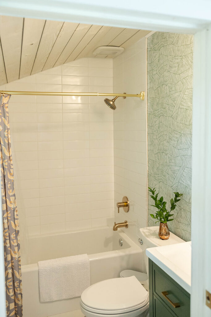 Renovated Cottage Bathroom with classic white subway tile, wallpaper and a wood ceiling.