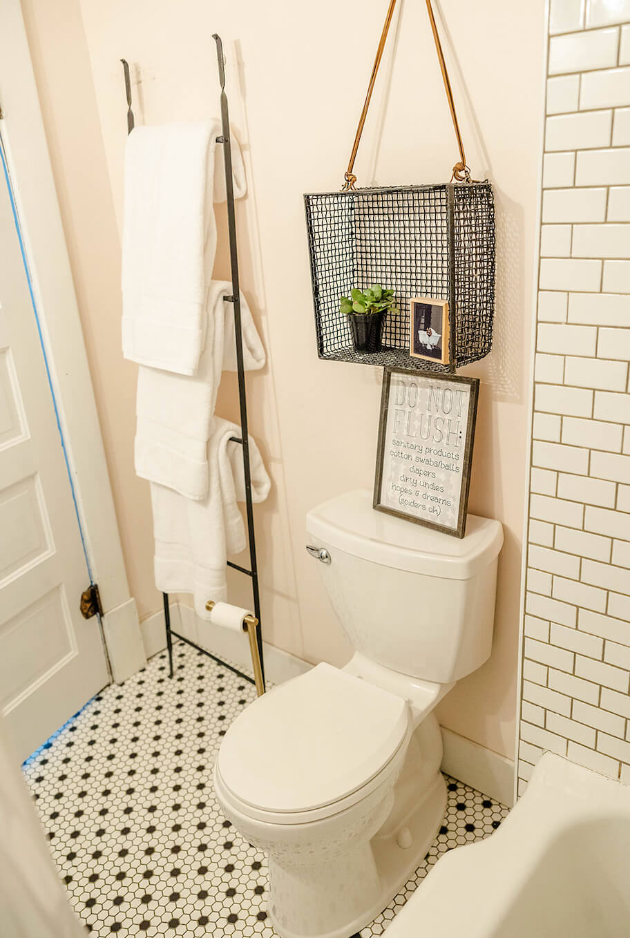 Renovated bathroom with pink walls and classic tile. Ladder holding towels. Pink floral wall decals.