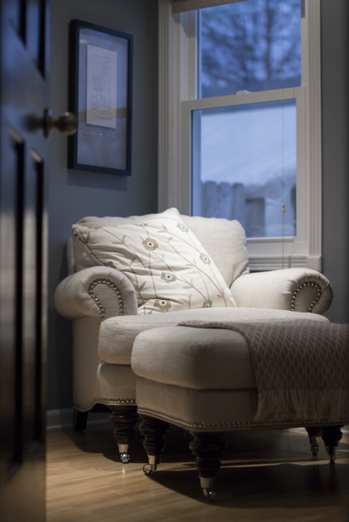 Cozy corner with cream colored chair and floral pillow with a throw.