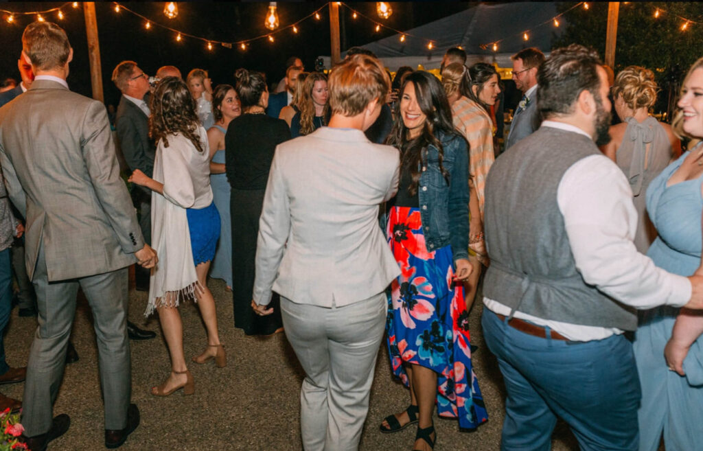 Wedding reception dance floor on an outdoor patio with string lights and guests are dancing.