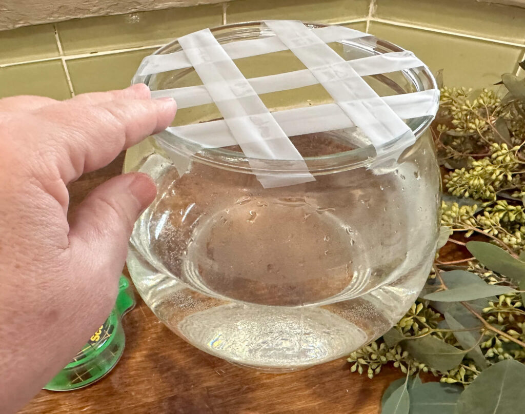 Round glass vase with a scotch tape grid for designing a floral arrangement.