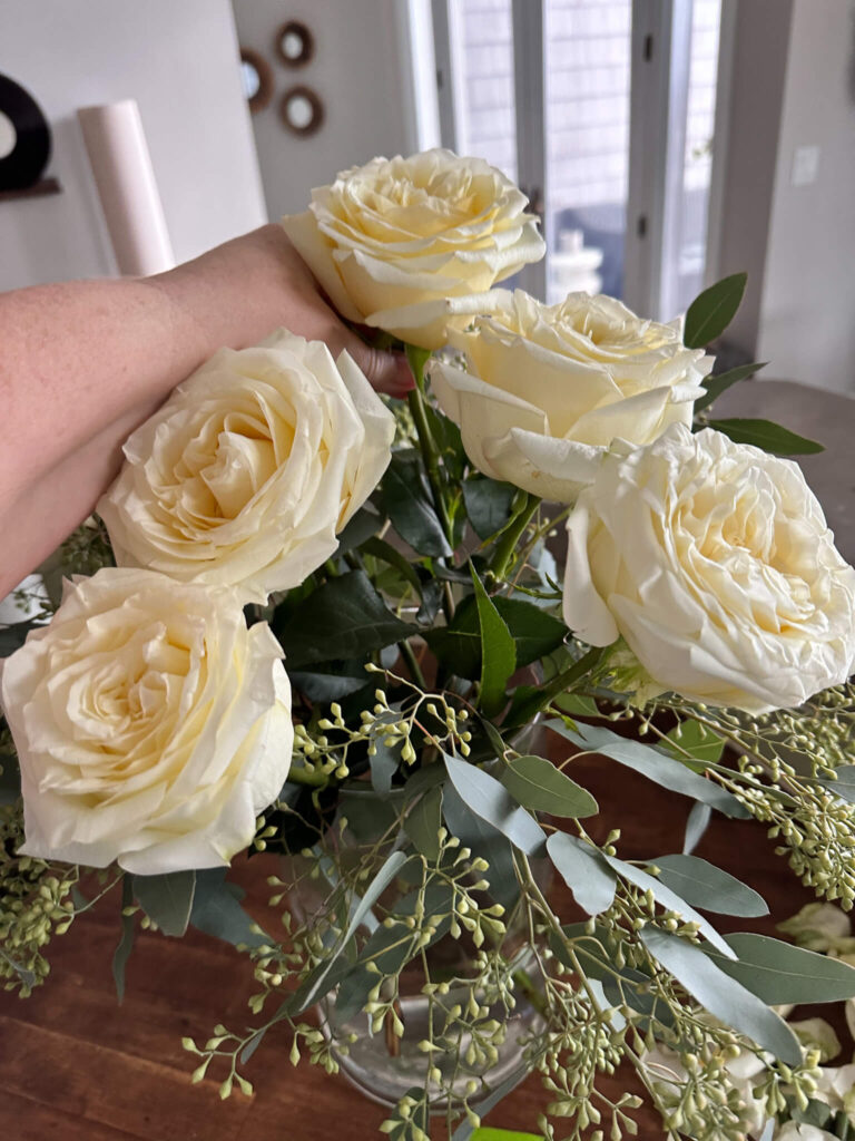 White Garden Roses being arranged in a clear vase.