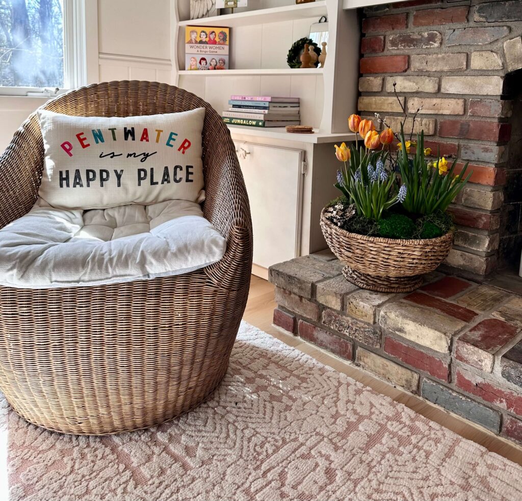 Cottage with a woven chair and a fireplace with a basket of spring bulbs in an arrangement.
