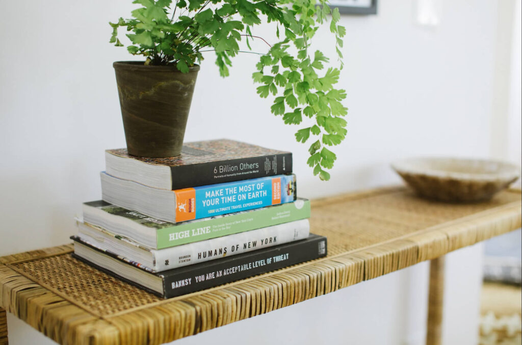 Rattan Table and a stack of coffee table books with a plant on top.