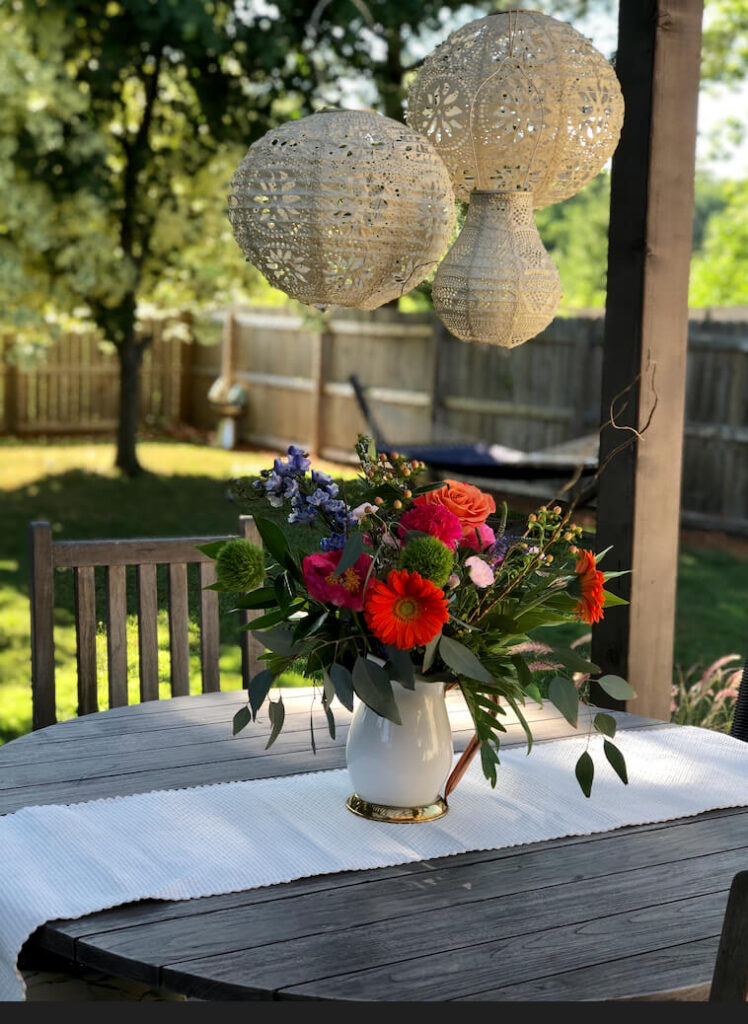 Solar lanterns hanging from a pergola. Fresh flowers on an outdoor table.