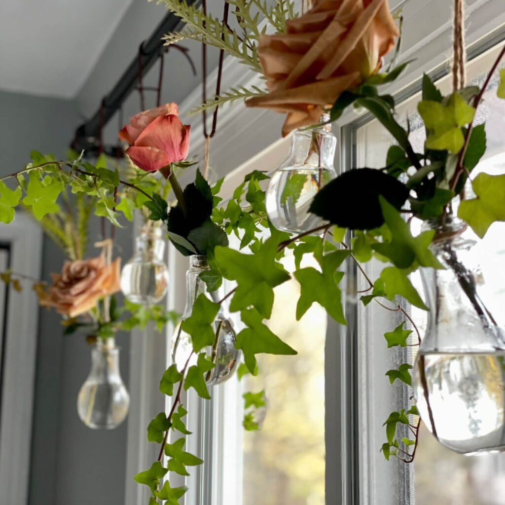 Vases with roses and vines in front of a window in a cottagecore bedroom.