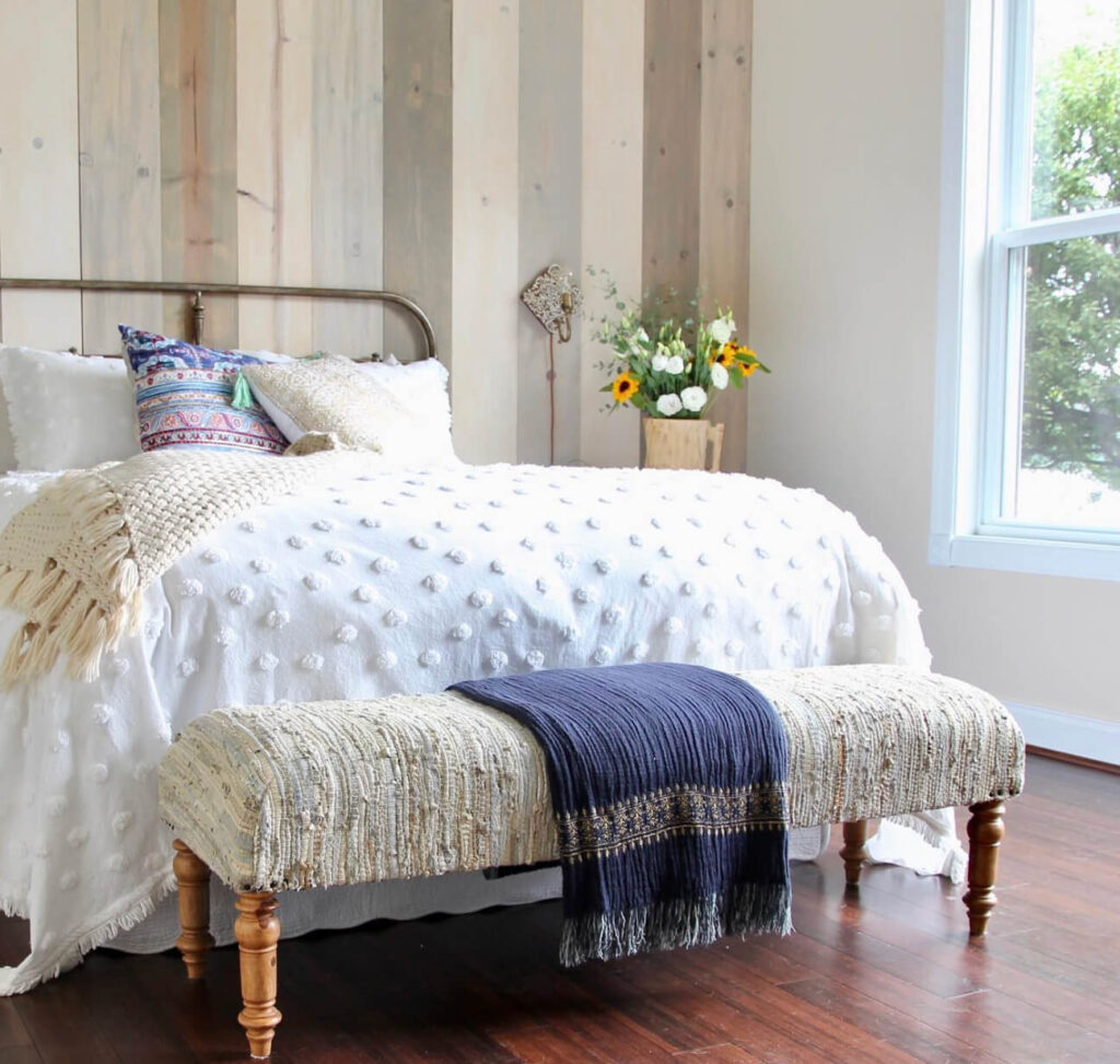 Wood plank  accent wall with a bed with a vintage headboard and layered quilts in a cottagecore bedroom.