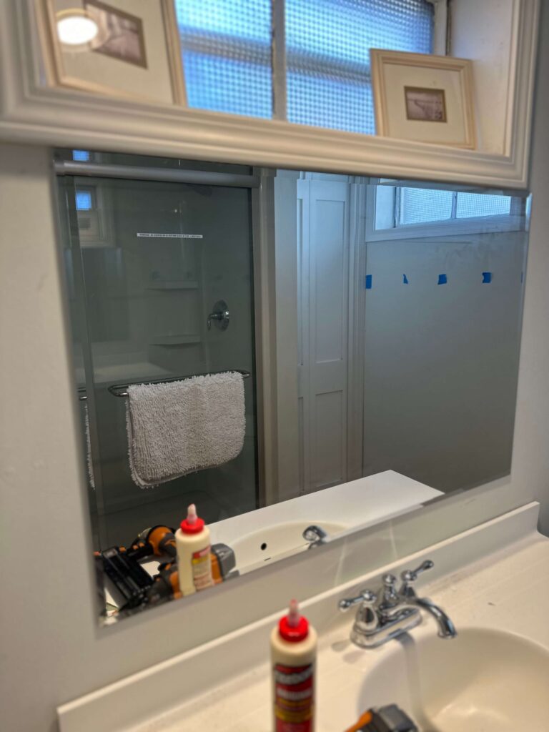 Adding a DIY Frame to a builder Grade Mirror in a Budget Bathroom Makeover.