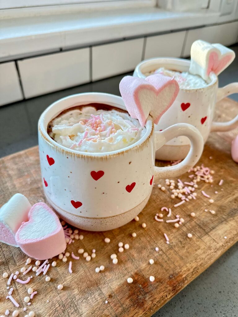 White mugs with red hearts filled with a Spiked Hot Chocolate Recipe for Galentine's Day