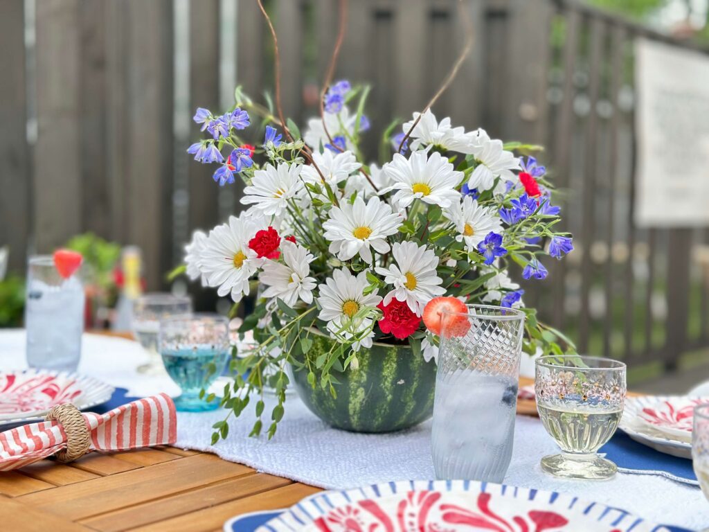 DIY Centerpiece using daisies, mini carnations, and delphinium, in a watermelon vase.