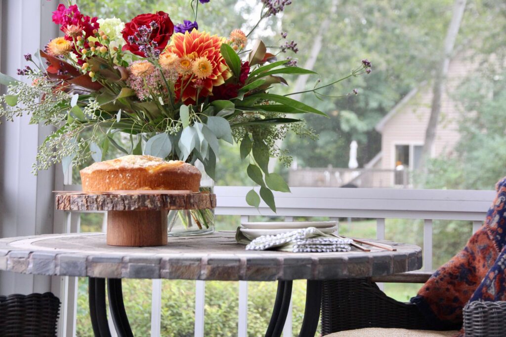 Fall flowers, apple coffee cake on a small outdfoor table.