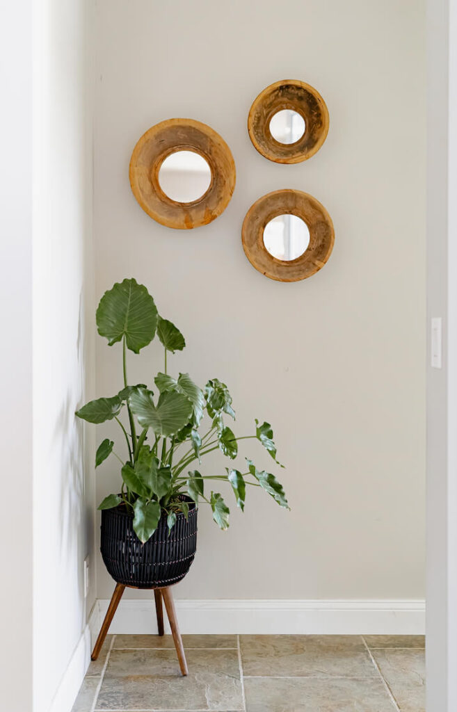 Three white oak round mirrors on a wall over a planter.