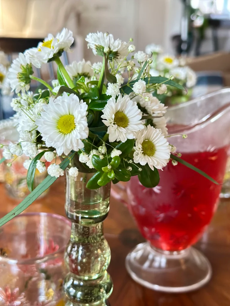 Close up of a green glass candlestick holder used as a vase for mini daisies and greenery on a spring tablescape
