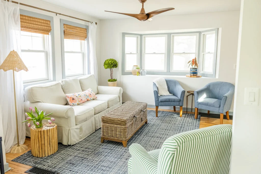Bright living area with white sofa and denim rug with green and white striped chair and ceiling fan.